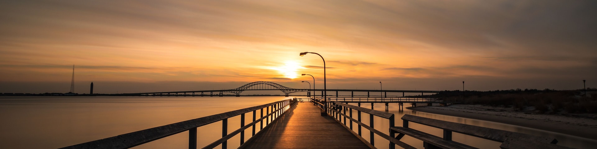 A wooden boardwalk leading to a bridge over calm water during sunset.