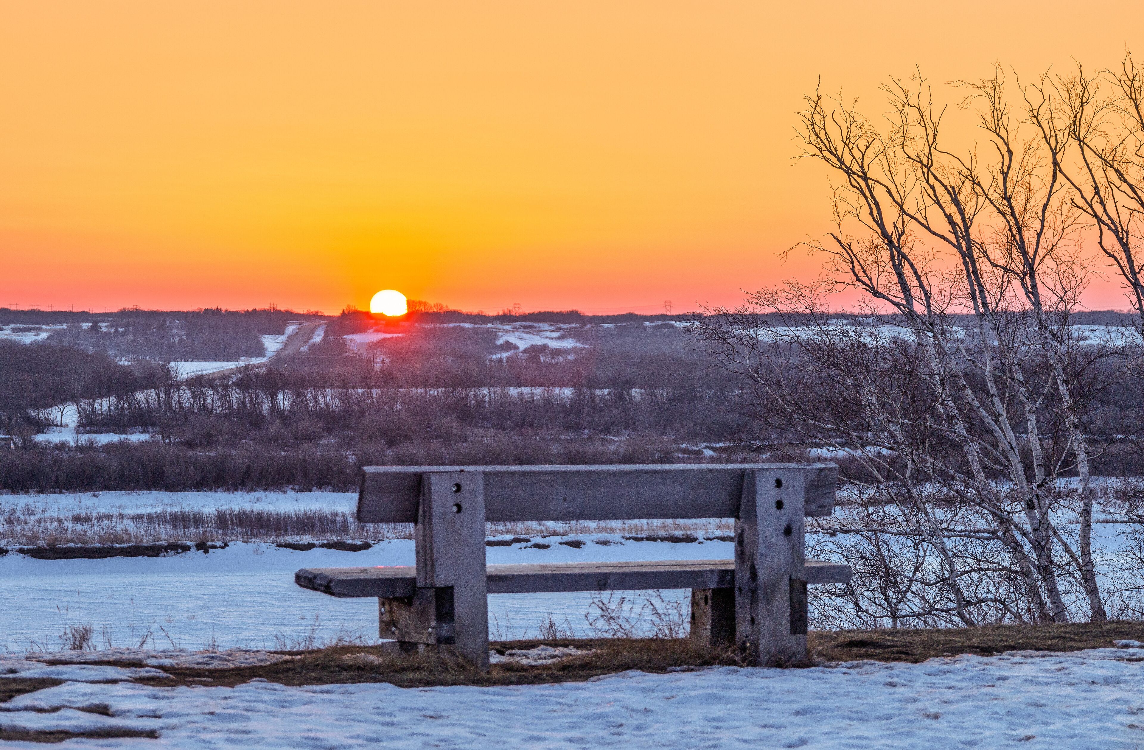 A bench overlooking a snowy landscape with a sunset in the background.