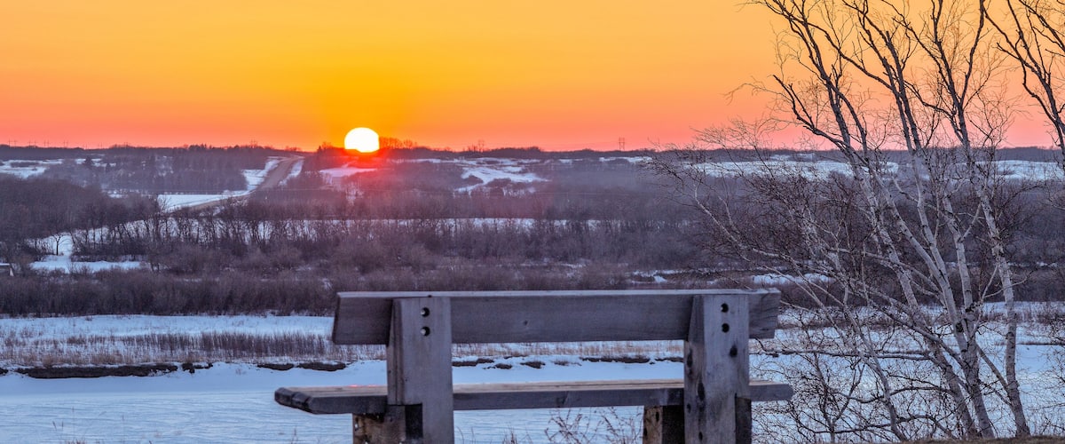 A bench overlooking a snowy landscape with a sunset in the background.