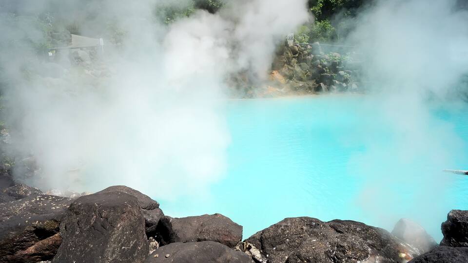 A geothermal hot spring with clear blue water surrounded by dark volcanic rocks.