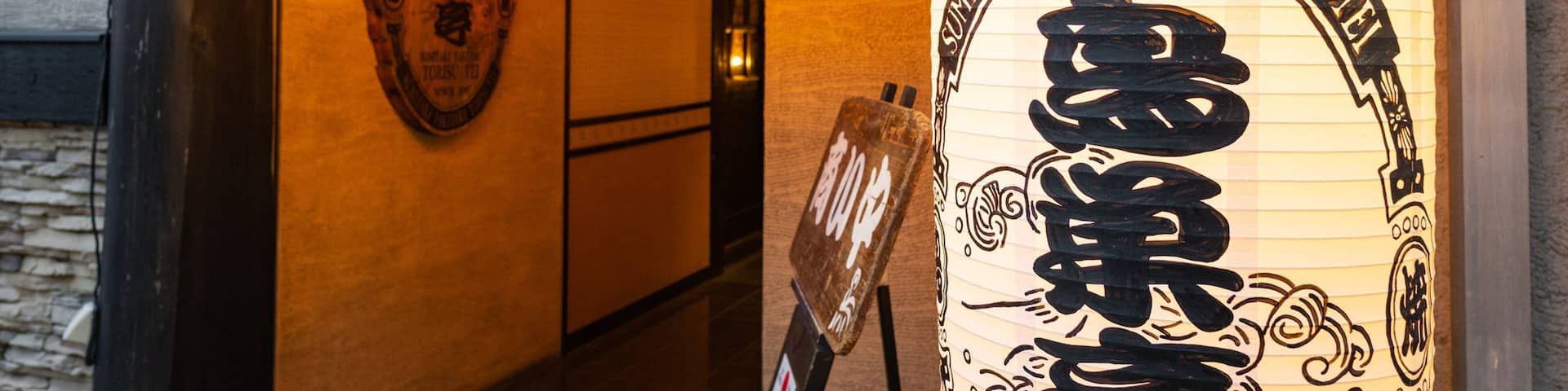 A traditional Japanese lantern with Japanese characters, a wooden sign with Japanese characters, and a row of hanging lanterns with Japanese characters.