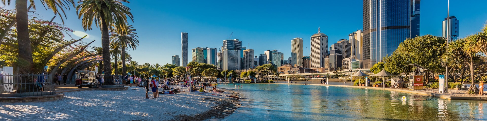 Un río con el horizonte de una ciudad al fondo, palmeras y gente en la orilla.