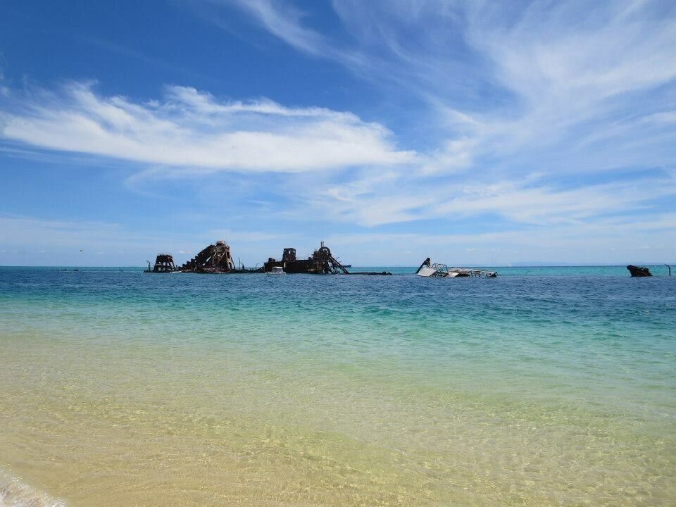 A clear turquoise sea with a sandy beach and several sunken ships.