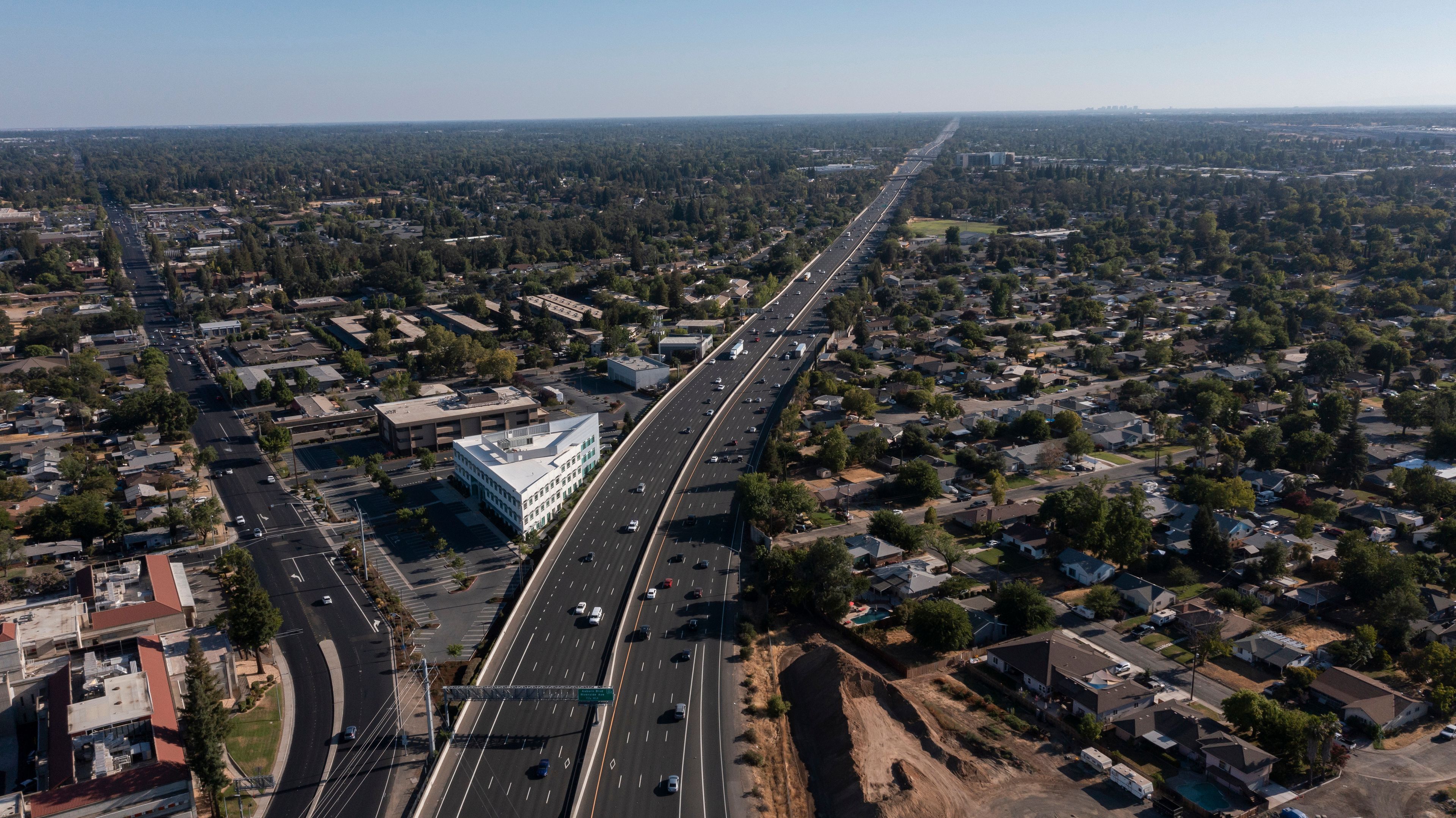 An aerial view of a highway cutting through a suburban area with residential houses and a large building.