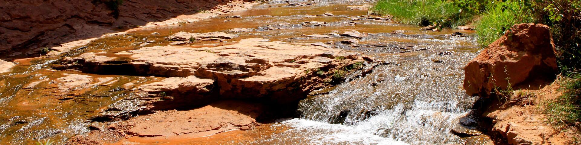 A river flowing through a canyon with red rock formations and green vegetation.