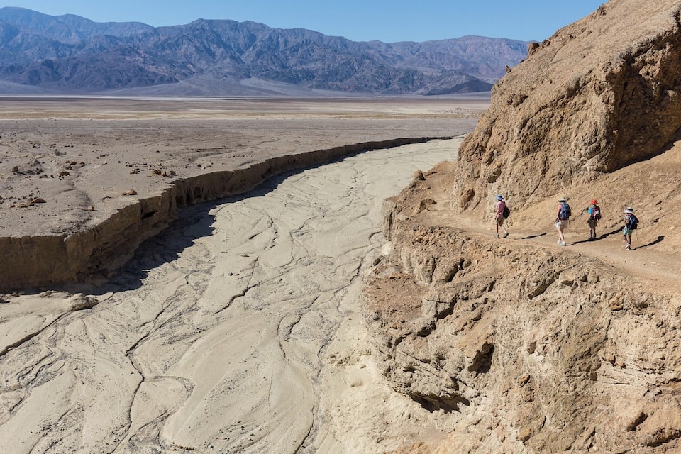 A group of hikers on a rocky trail with a vast desert landscape and mountains in the background.