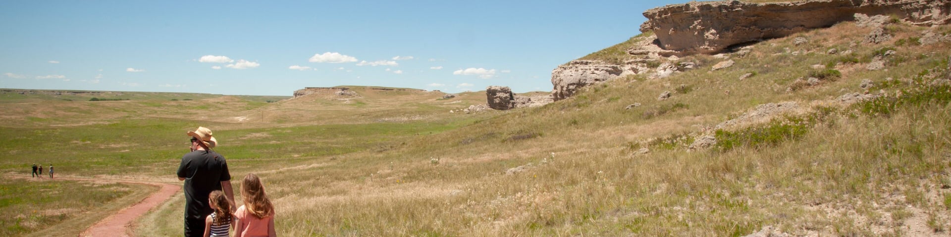 A red path in a grassy field with a rocky cliff in the background.