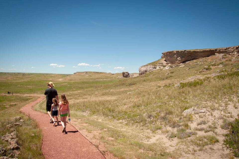 A red path in a grassy field with a rocky cliff in the background.