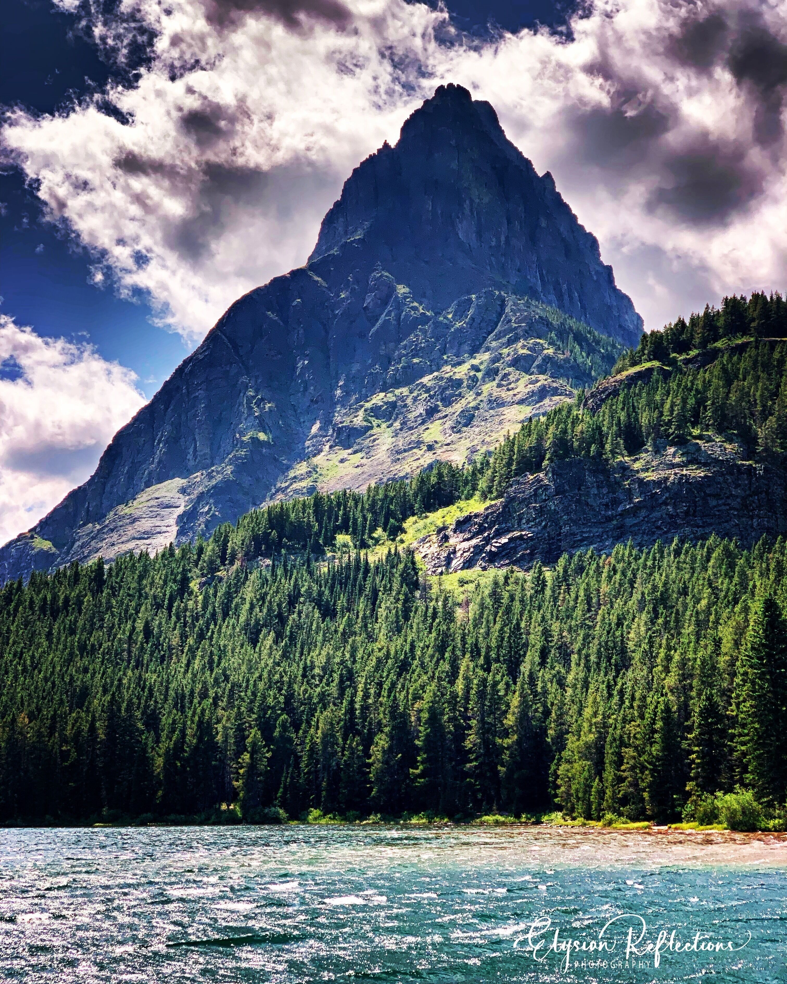 A mountain with a forested slope and a river in the foreground.