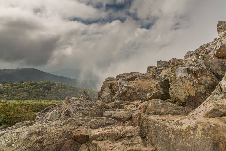 Paisaje montañoso rocoso con vegetación verde exuberante y un cielo nublado.