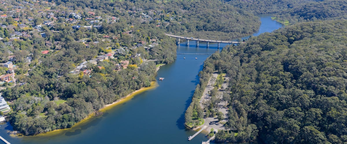 A river with a bridge, surrounded by dense forest and residential areas.