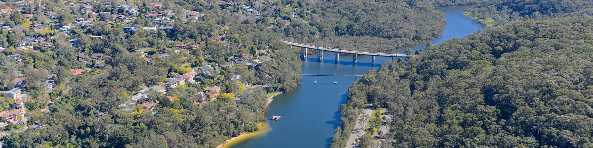 A river with a bridge, surrounded by dense forest and residential areas.