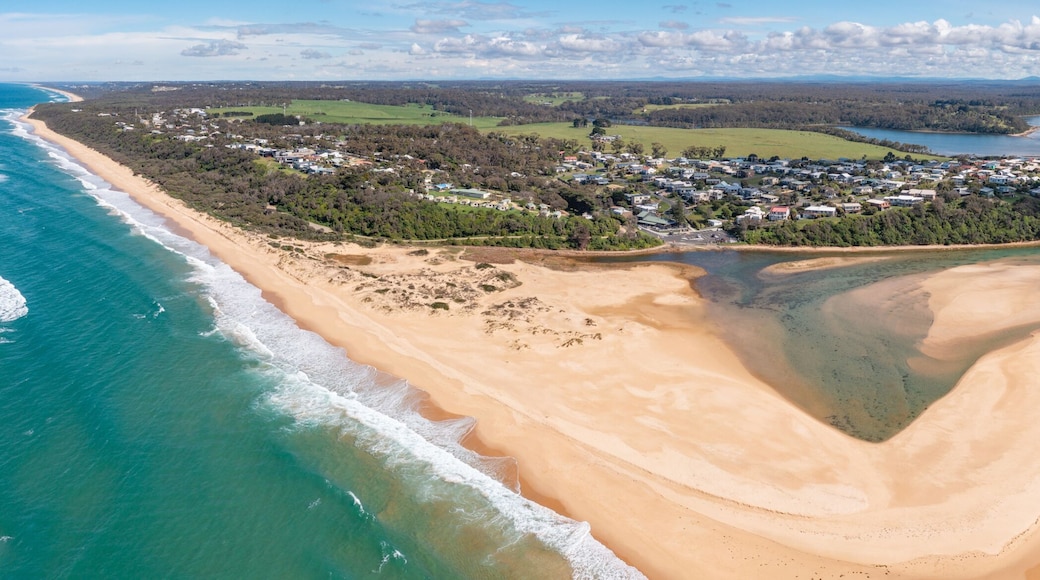An aerial view of a coastal town with a beach, clear waters, and surrounding greenery.