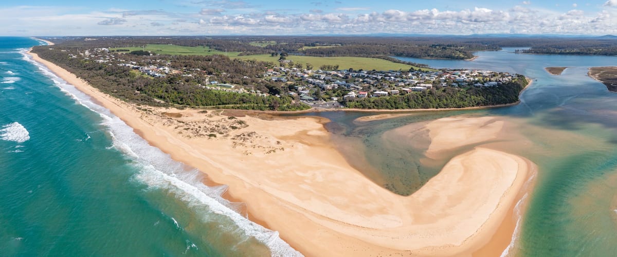 An aerial view of a coastal town with a beach, clear waters, and surrounding greenery.