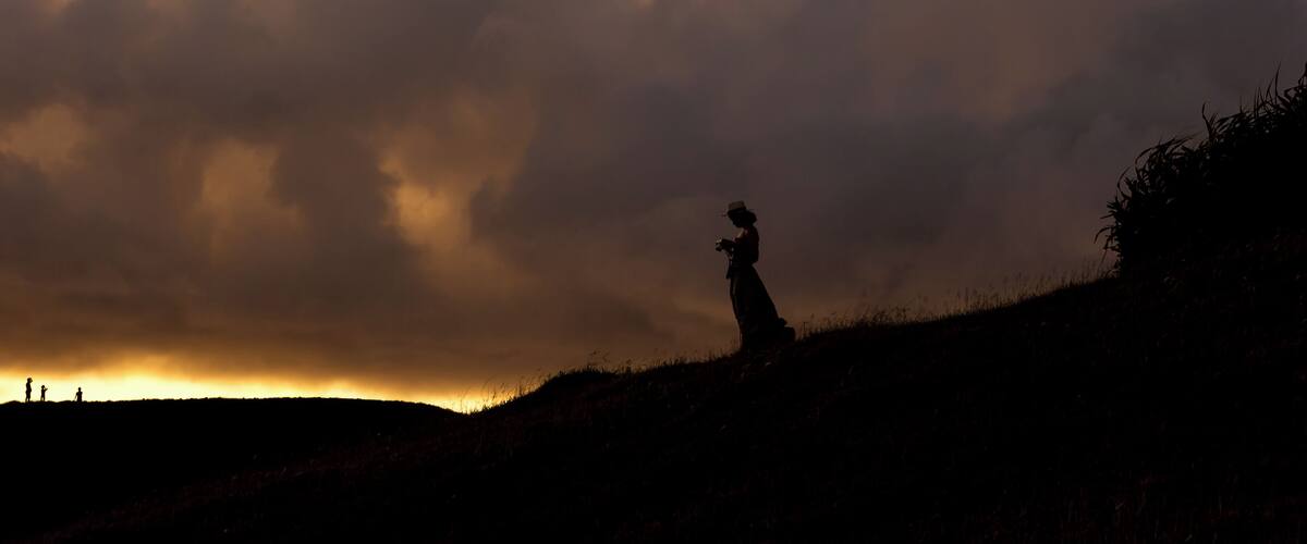 A silhouette of a person on a hill with a dramatic sky.