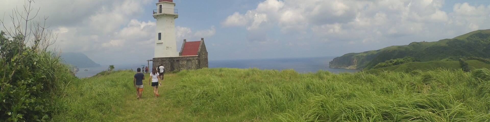 A lighthouse on a grassy hill with a red roof, overlooking the sea.