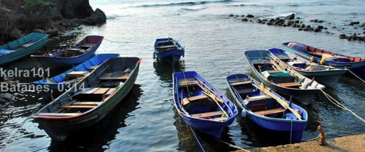 Several small boats tied to a rocky shore by the sea.