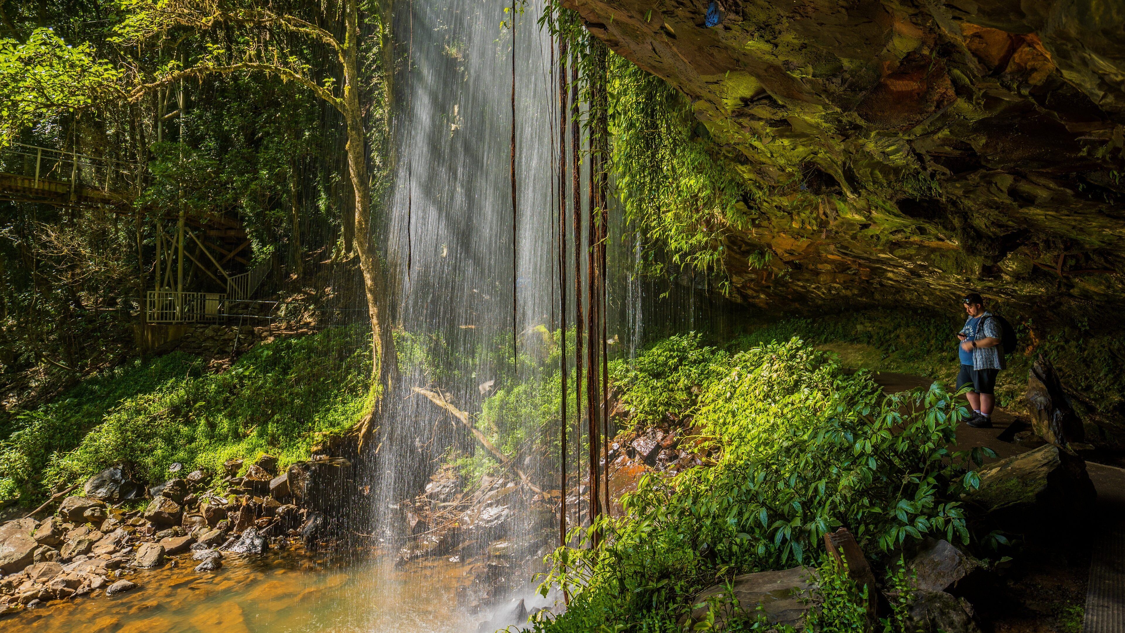 Ein Wasserfall in bewaldeter Landschaft, in der Nähe steht eine Person.