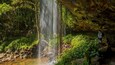 A waterfall in a forested area with a person standing nearby.