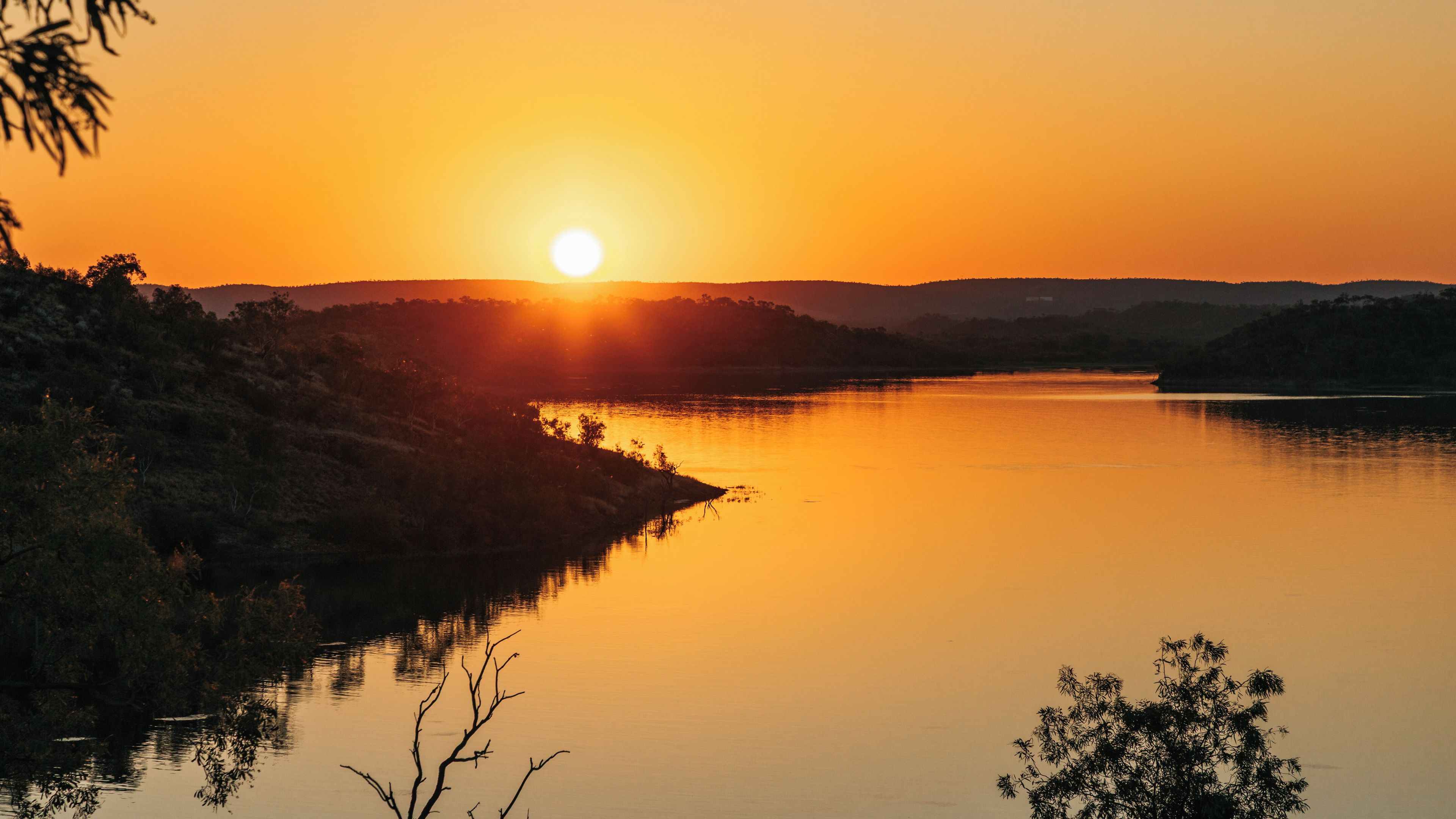 A sunset over a calm lake with silhouetted hills in the background.