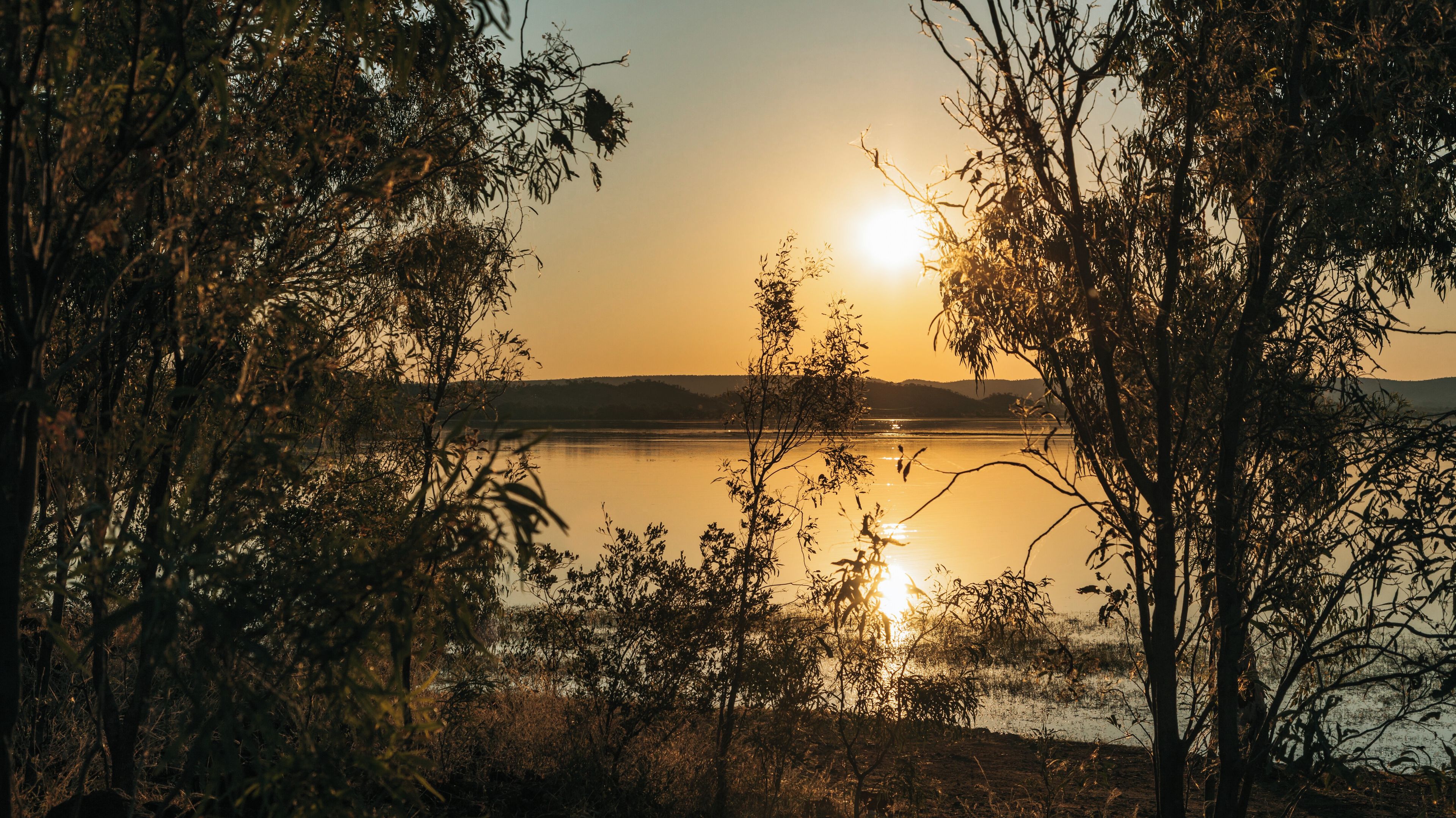 A sunset over a calm lake with trees in the foreground.
