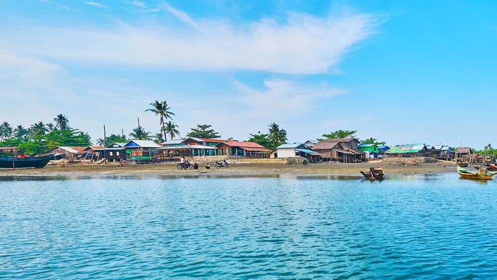A coastal village with boats, houses, and palm trees.