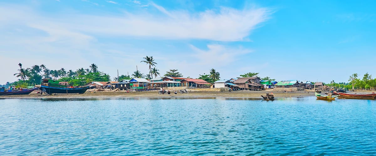 A coastal village with boats, houses, and palm trees.