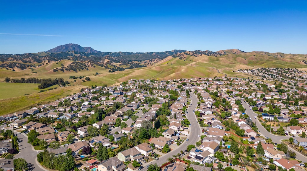 Closer aerial view of residential homes in Antioch, CA featuring landscaped backyards, driveways, solar panels, and hillside roads in a well-maintained suburban setting