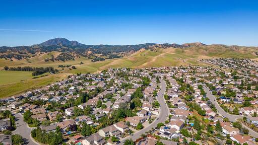 Closer aerial view of residential homes in Antioch, CA featuring landscaped backyards, driveways, solar panels, and hillside roads in a well-maintained suburban setting