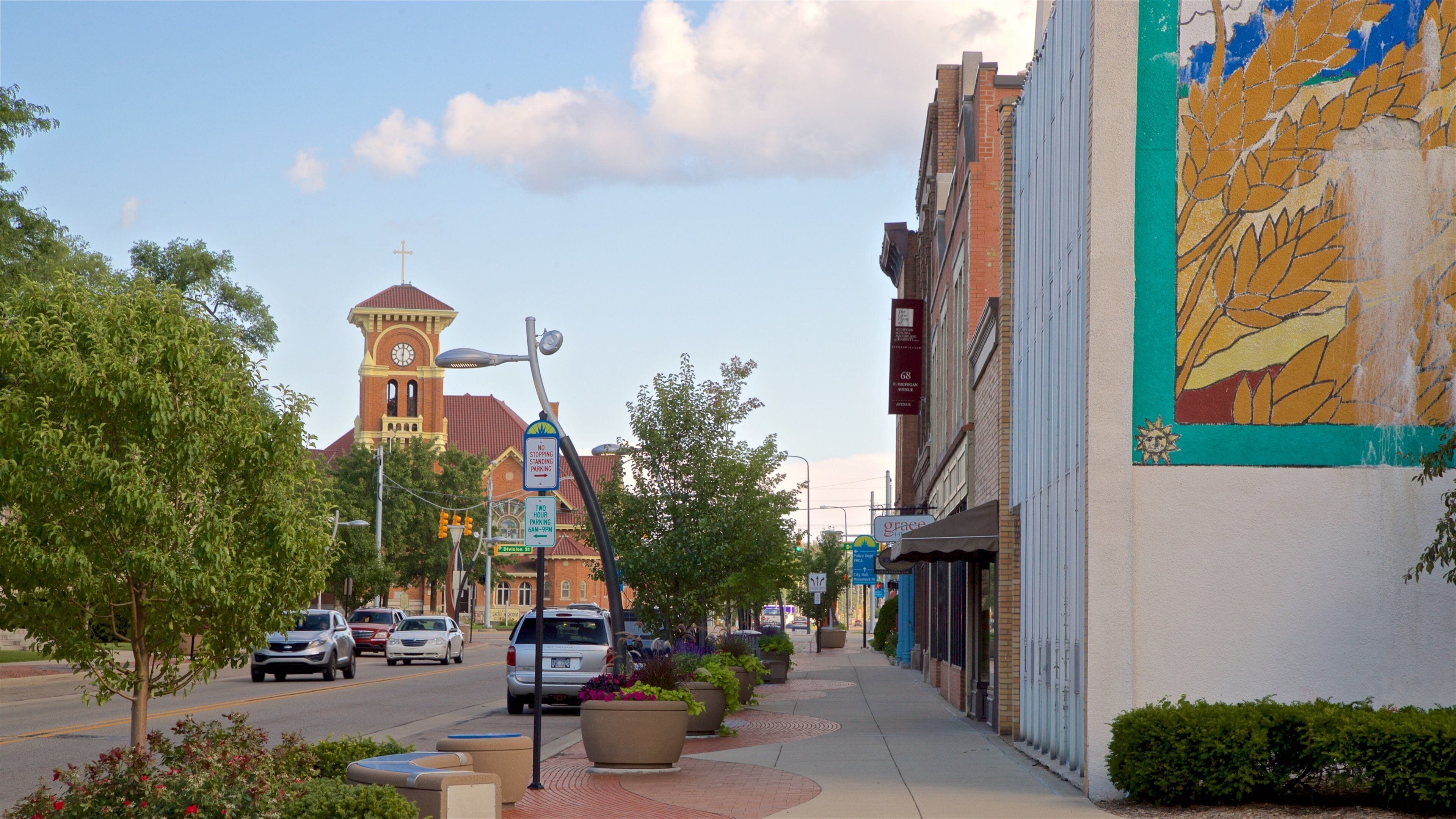 A street with a clock tower, a mural, and parked cars.