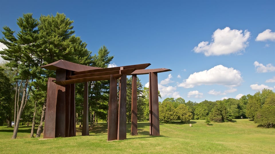 A metal sculpture in a grassy field with trees in the background.