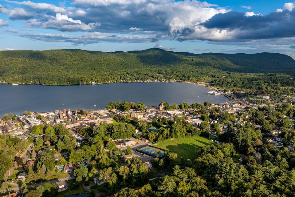 A lakeside town with a large body of water, dense forests, and rolling hills in the background.