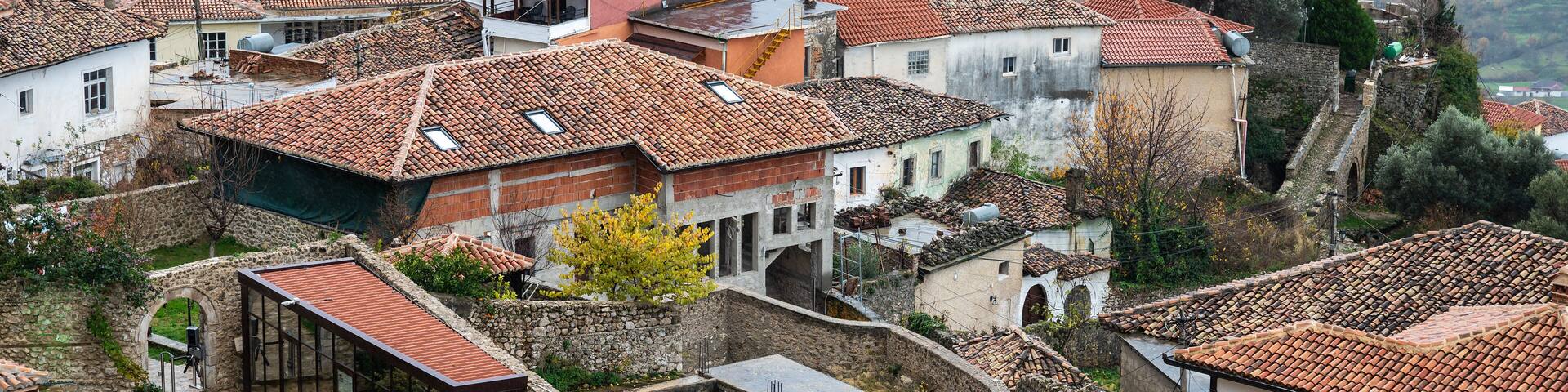 A historic village with terracotta-roofed buildings, stone walls, and a prominent tower.
