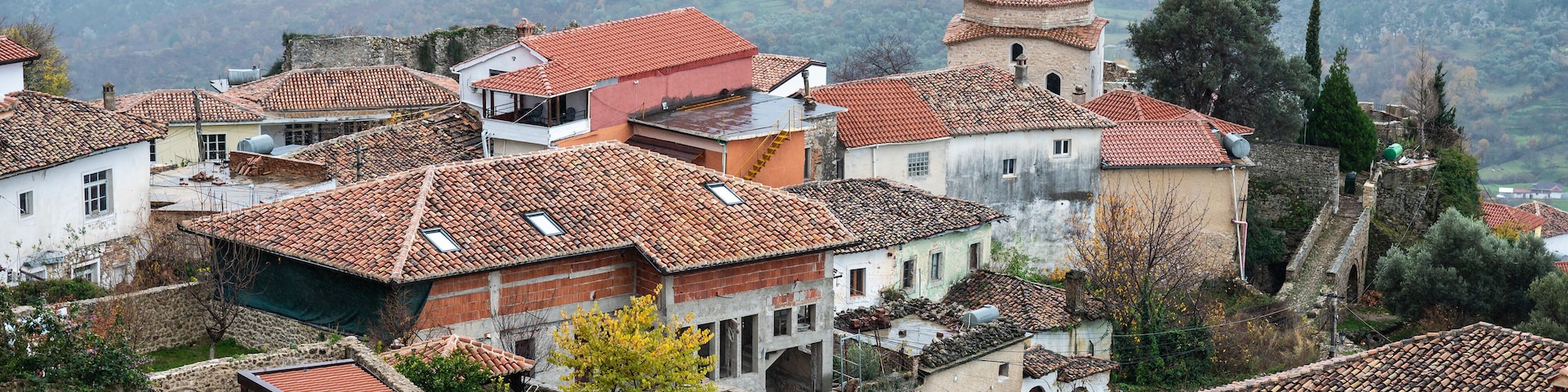 A historic village with terracotta-roofed buildings, stone walls, and a prominent tower.