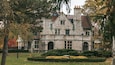 A large stone building with a steep roof, surrounded by trees and a well-maintained garden.