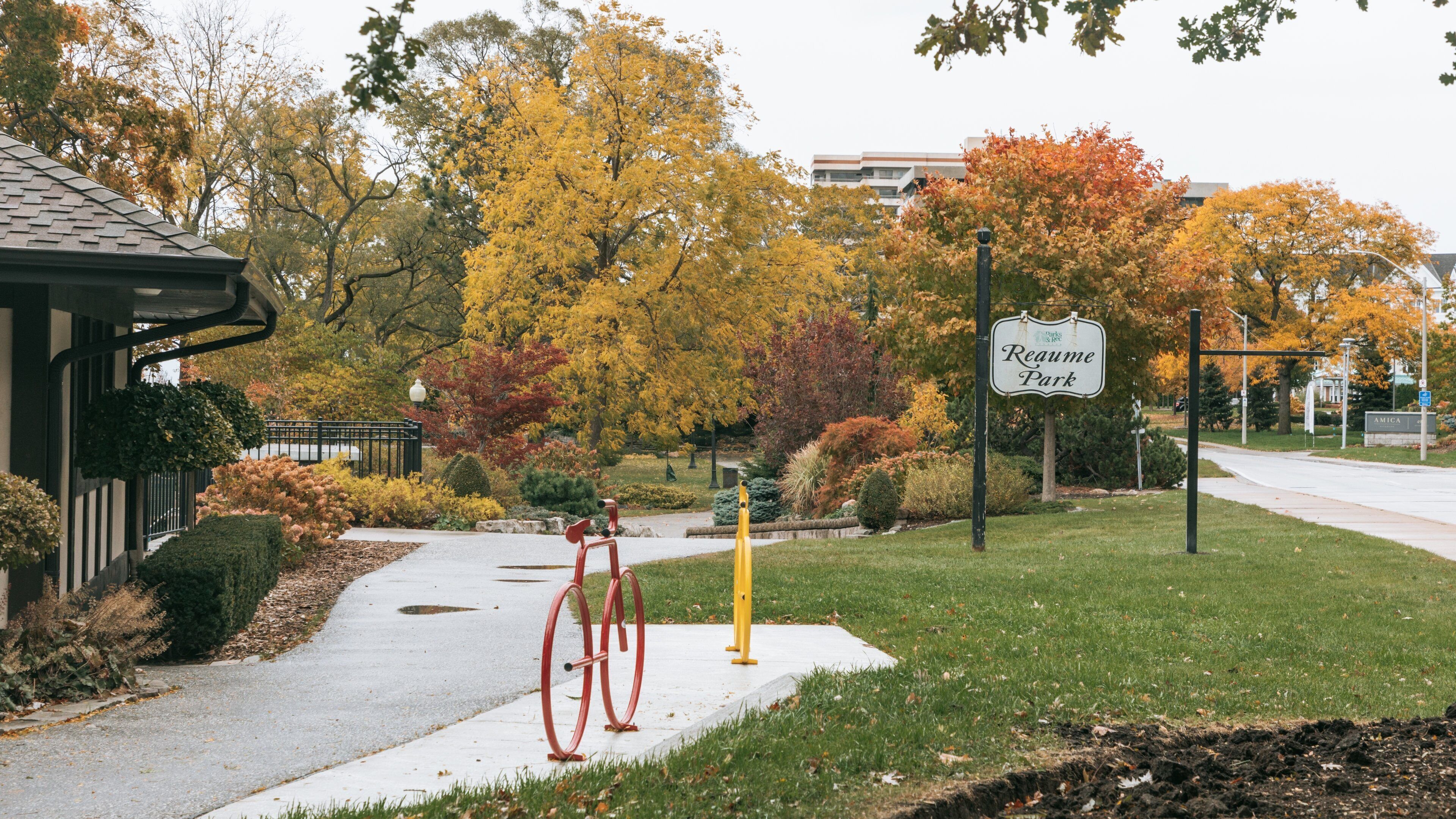 A park entrance with a sign reading "Reame Park," surrounded by autumn-colored trees and a red bicycle.