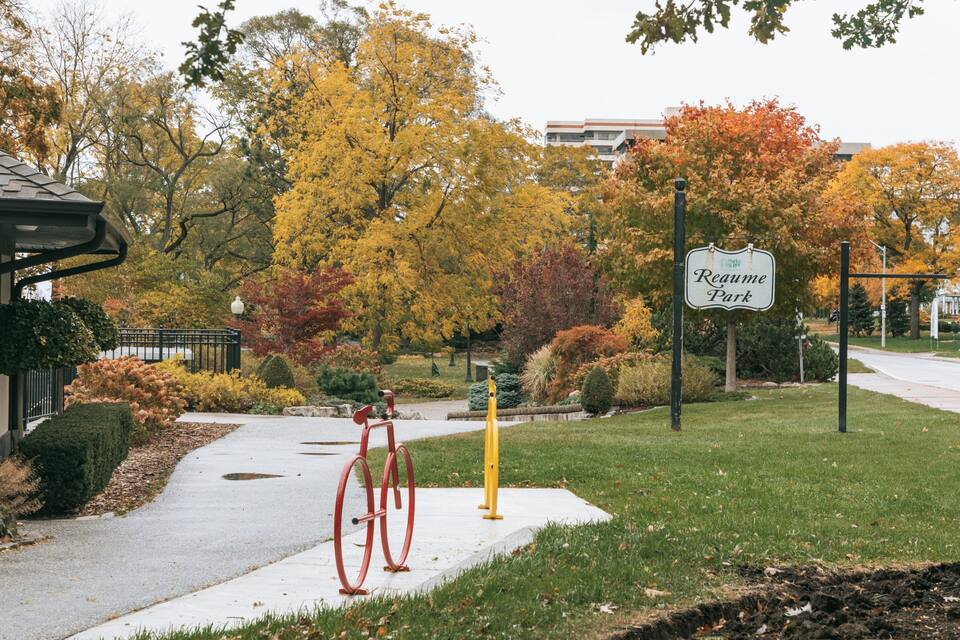 A park entrance with a sign reading "Reame Park," surrounded by autumn-colored trees and a red bicycle.