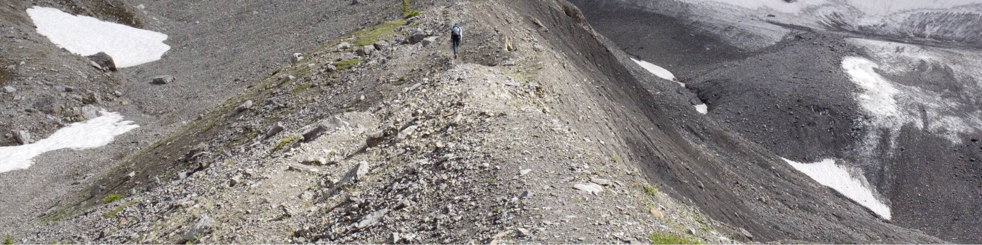 A rugged mountain landscape with snow patches and a rocky path.