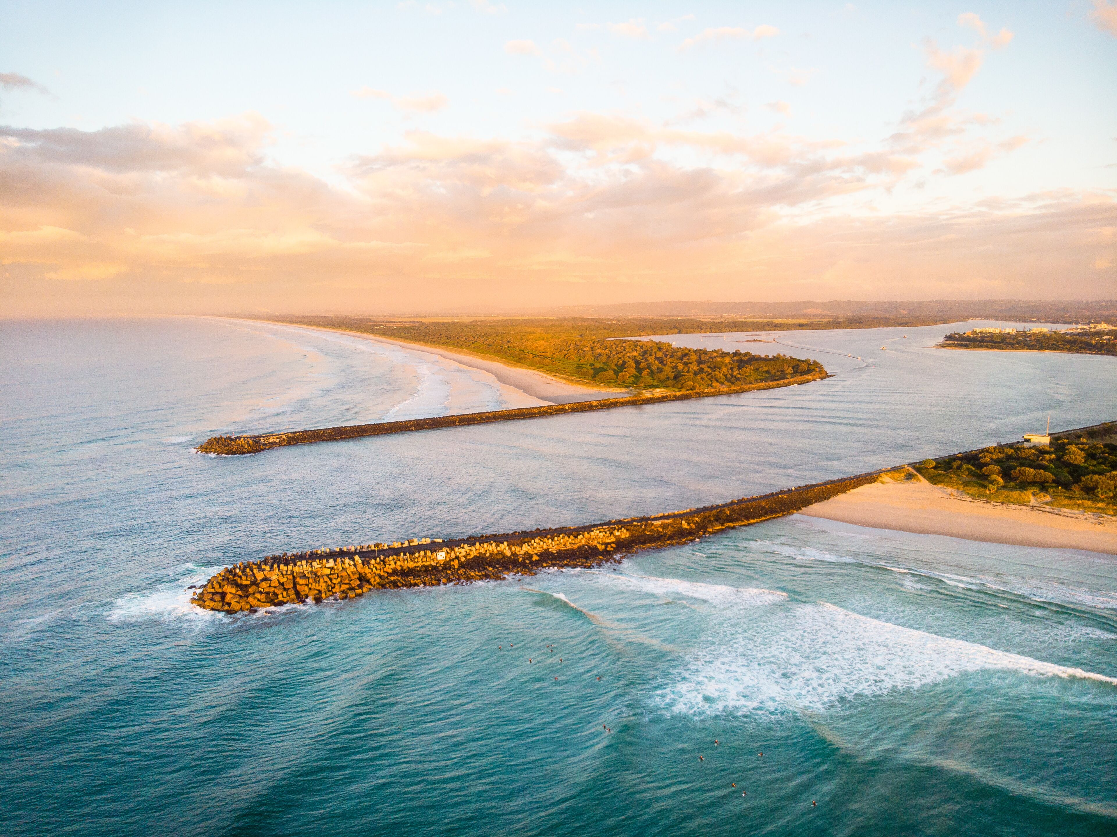 A coastal landscape with a long breakwater, sandy beaches, and a clear sky.