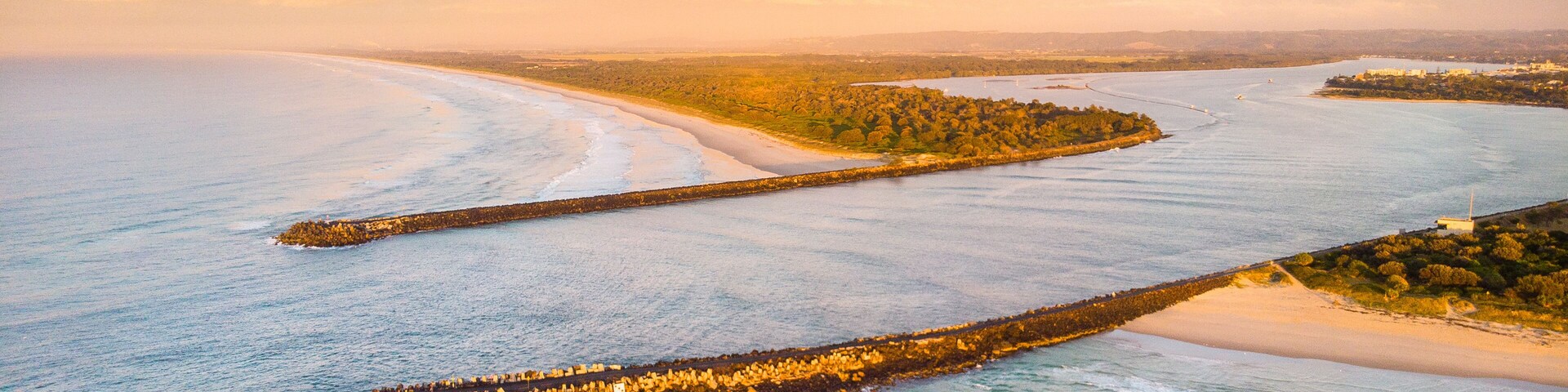 A coastal landscape with a long breakwater, sandy beaches, and a clear sky.