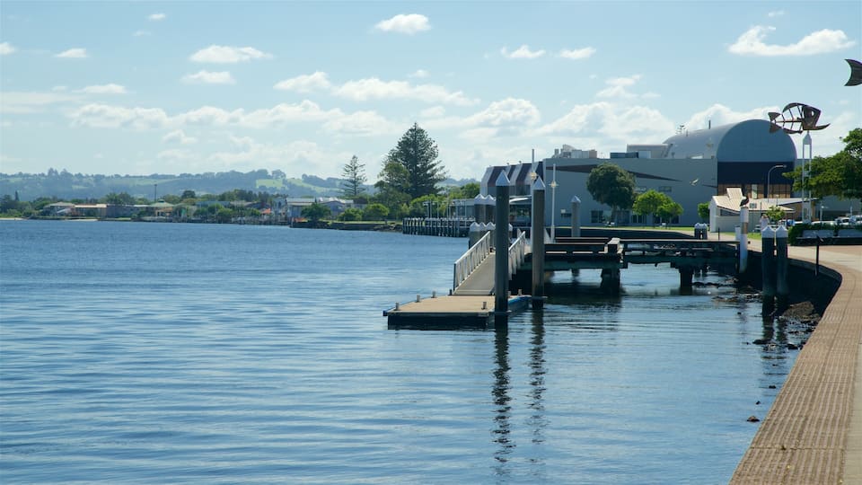 A waterfront with a pier, a modern building with a dome, and a clear sky.