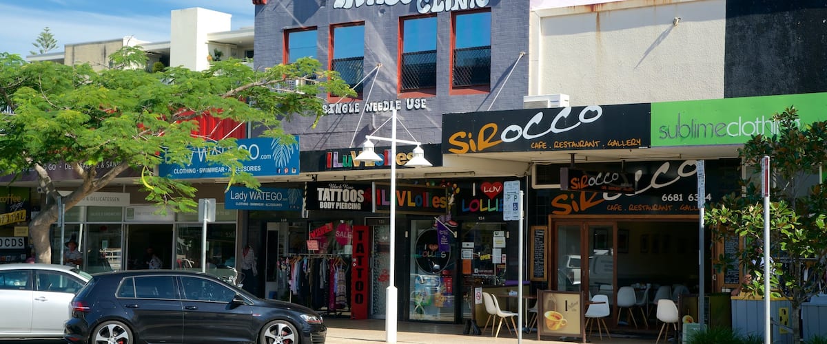 A tattoo clinic, a cafe, and a clothing store on a sunny street.