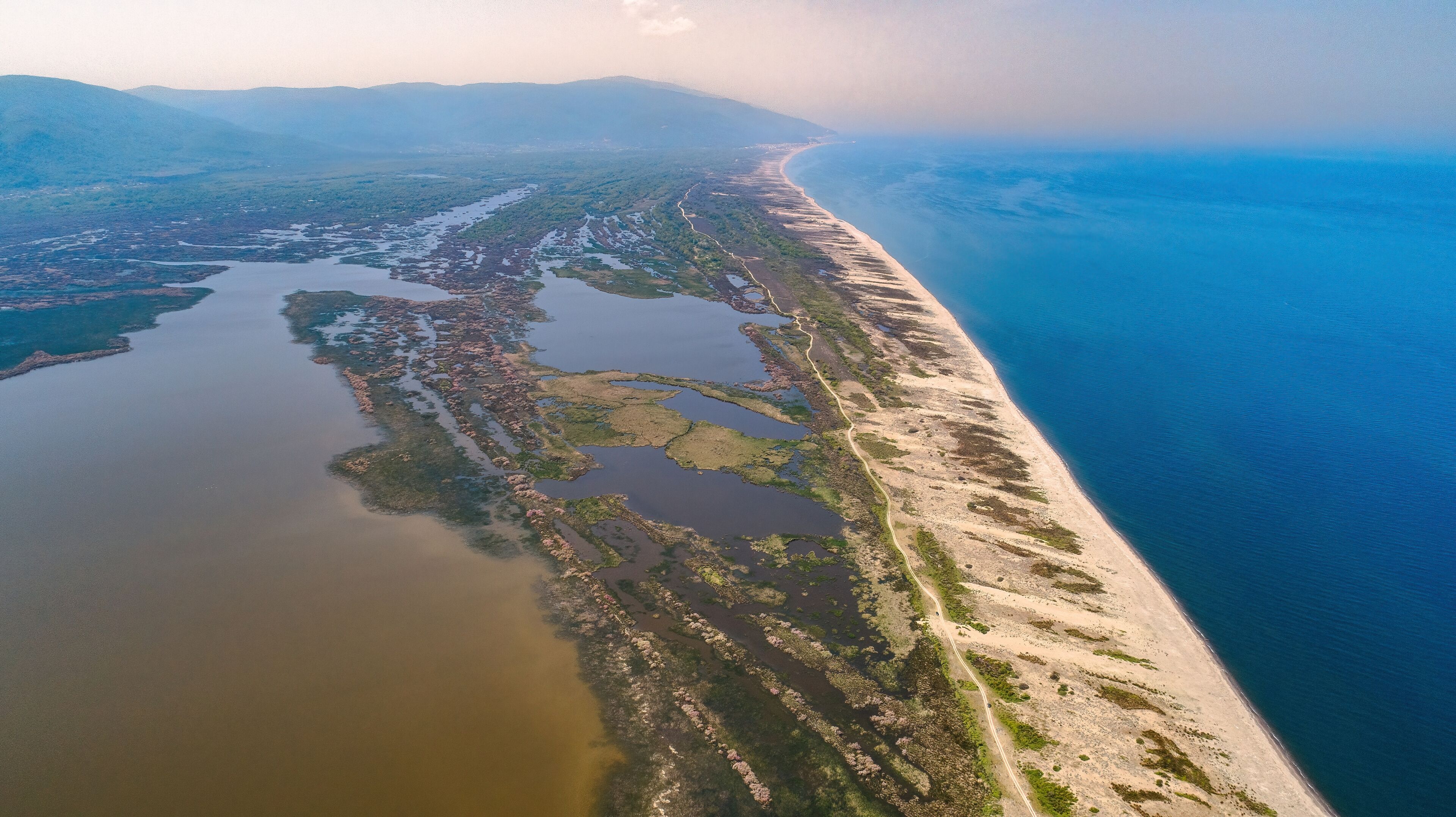 A coastal landscape with a sandy beach, a river or estuary, and distant mountains.