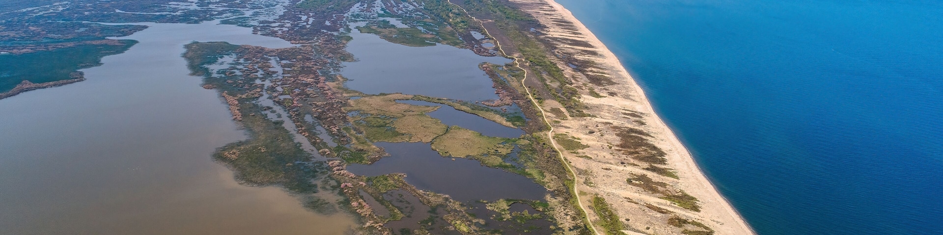 A coastal landscape with a sandy beach, a river or estuary, and distant mountains.