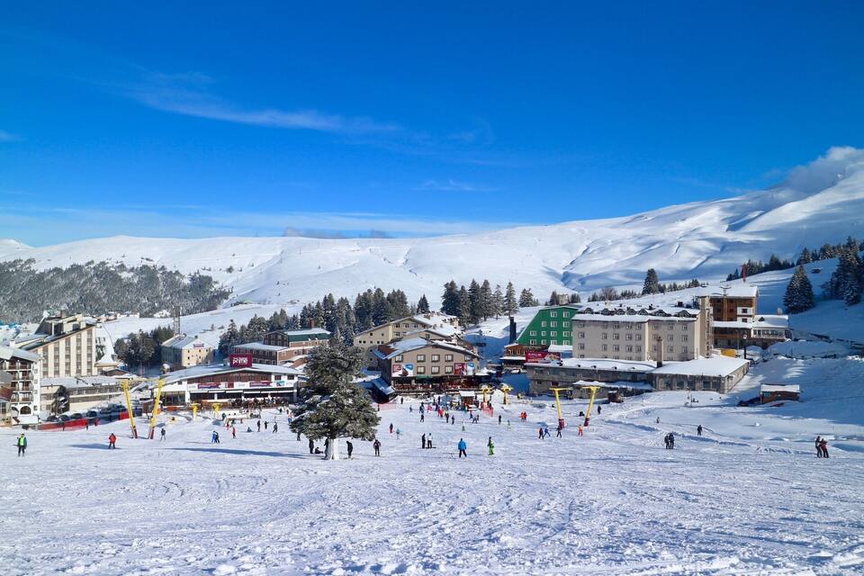 Ein schneebedecktes Skigebiet mit Gebäuden, einer Seilbahn und einem Berg im Hintergrund.