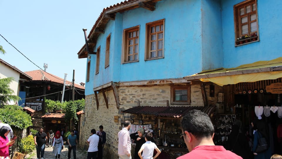 A blue building with a stone base, a tiled roof, and a shop with various items on display.