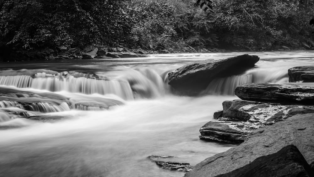 A river with a smooth, flowing water surface, surrounded by rocks and dense foliage.