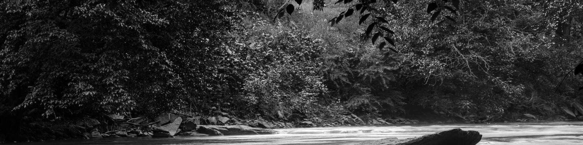 A river with a smooth, flowing water surface, surrounded by rocks and dense foliage.