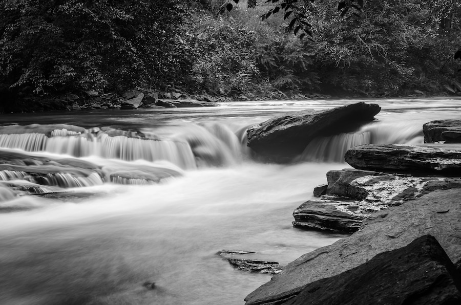 A river with a smooth, flowing water surface, surrounded by rocks and dense foliage.