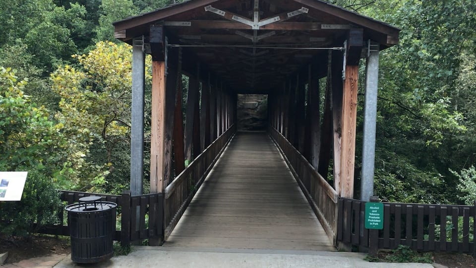 Un ponte di legno coperto in una zona boschiva, con un cartello che vieta alcol e tabacco.